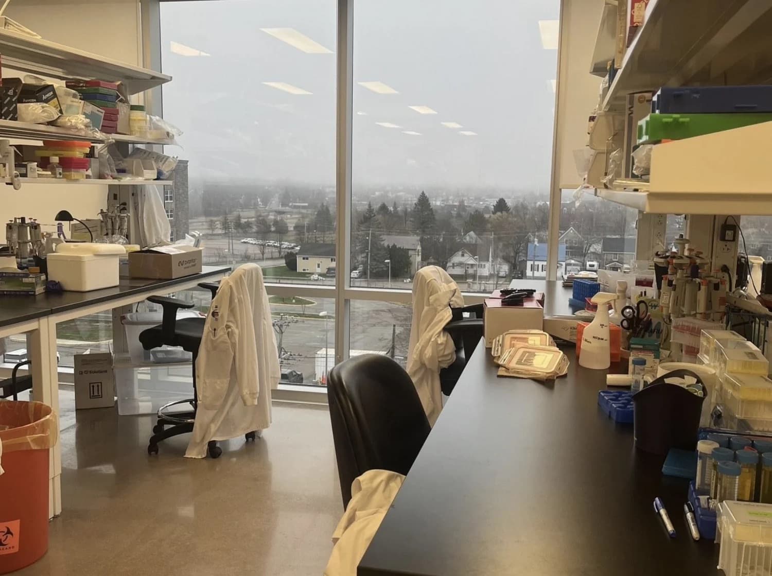 A diagnostics laboratory with benches, pipettes and lab coats by large windows